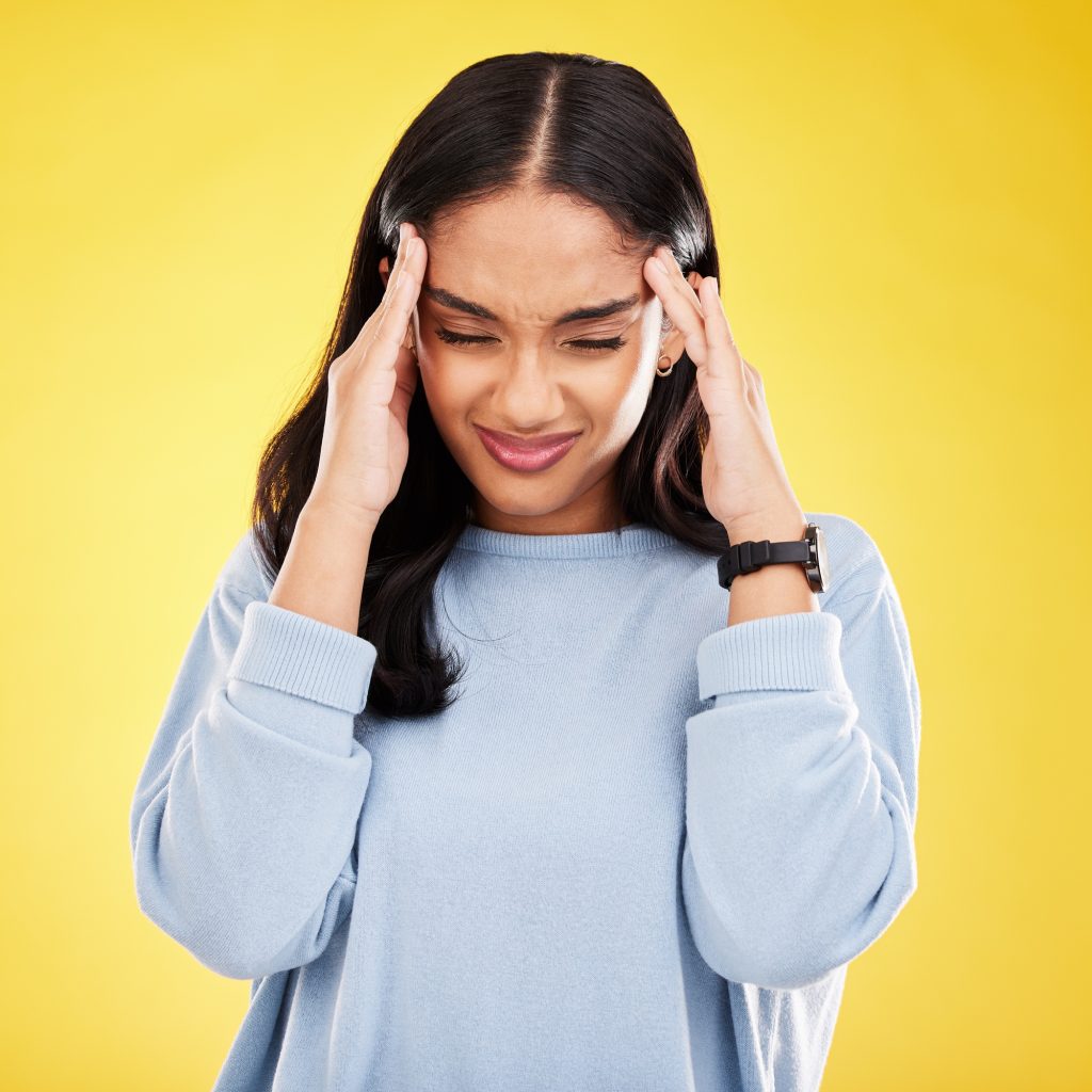 Young woman, stress and burnout with headache, pain and distress isolated on yellow studio backgrou